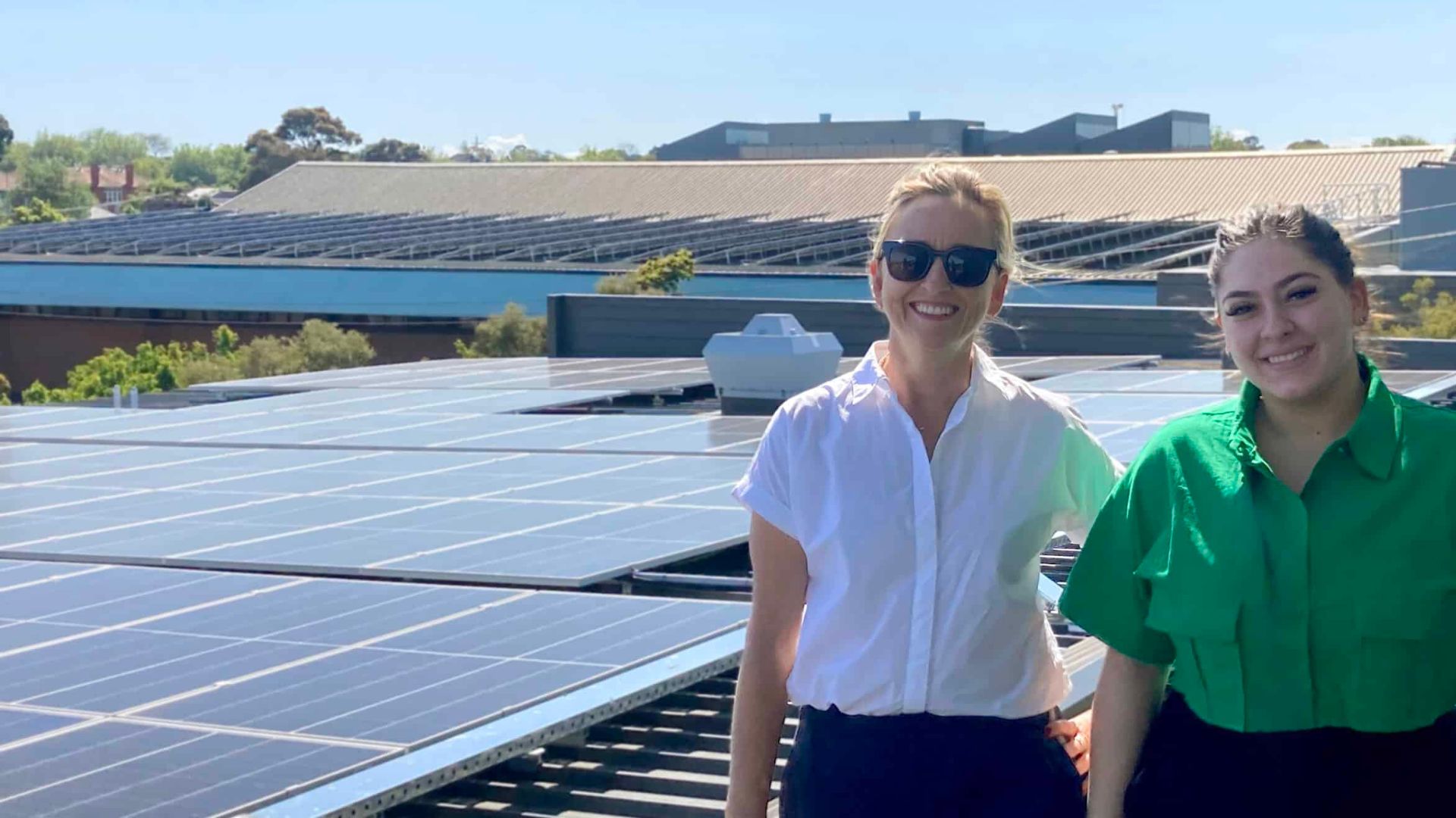 Two women: Annabel Jarvis and Anna stand next to roof with solar panels